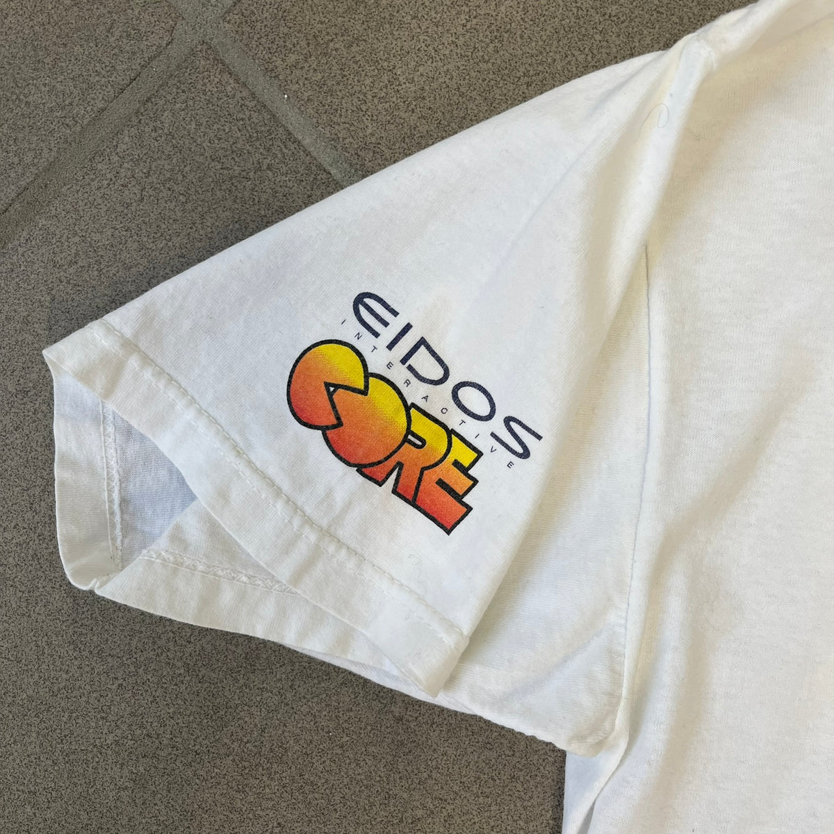 Tomb Raider III 1998 “Lara’s Back” White Tee is a boxy white T-shirt made on a Sierra Teez blank, with a stone-styled Tomb Raider III: Adventures of Lara Croft logo on the front. The back has a low-poly graphic of Lara Croft ass with “Lara’s Back...” text underneath, and the sleeve carries Eidos and Core logos.