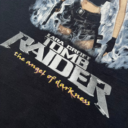 Tomb Raider: The Angel of Darkness 2003 Tee is a black washed T-shirt featuring a small game logo on the front chest. The back displays a large graphic based on the game cover, with Lara Croft in front of a flame rendered in early 3D-style artwork, with the game title printed below.
