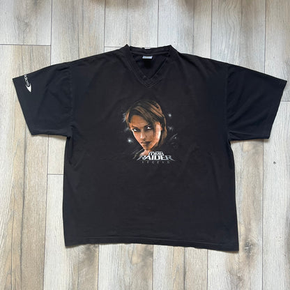 Tomb Raider Lara Croft 2006 Legend Tee is a black V-neck T-shirt made from 100% cotton on a Hanes blank. The front features the Lara Croft: Tomb Raider Legend cover graphic with Lara Croft’s face and the game title printed below. A white Eidos logo is printed on the sleeve, referencing the official game publisher.
