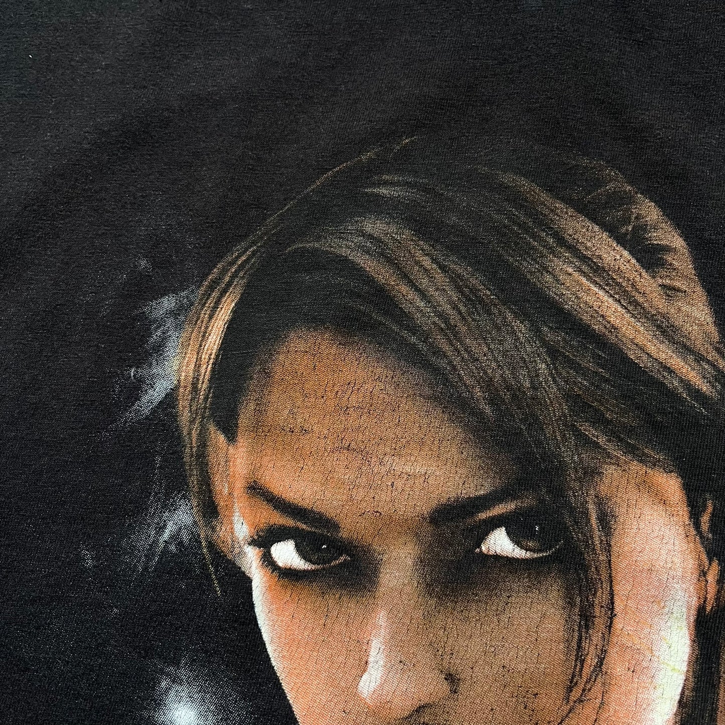 Tomb Raider Lara Croft 2006 Legend Tee is a black V-neck T-shirt made from 100% cotton on a Hanes blank. The front features the Lara Croft: Tomb Raider Legend cover graphic with Lara Croft’s face and the game title printed below. A white Eidos logo is printed on the sleeve, referencing the official game publisher.
