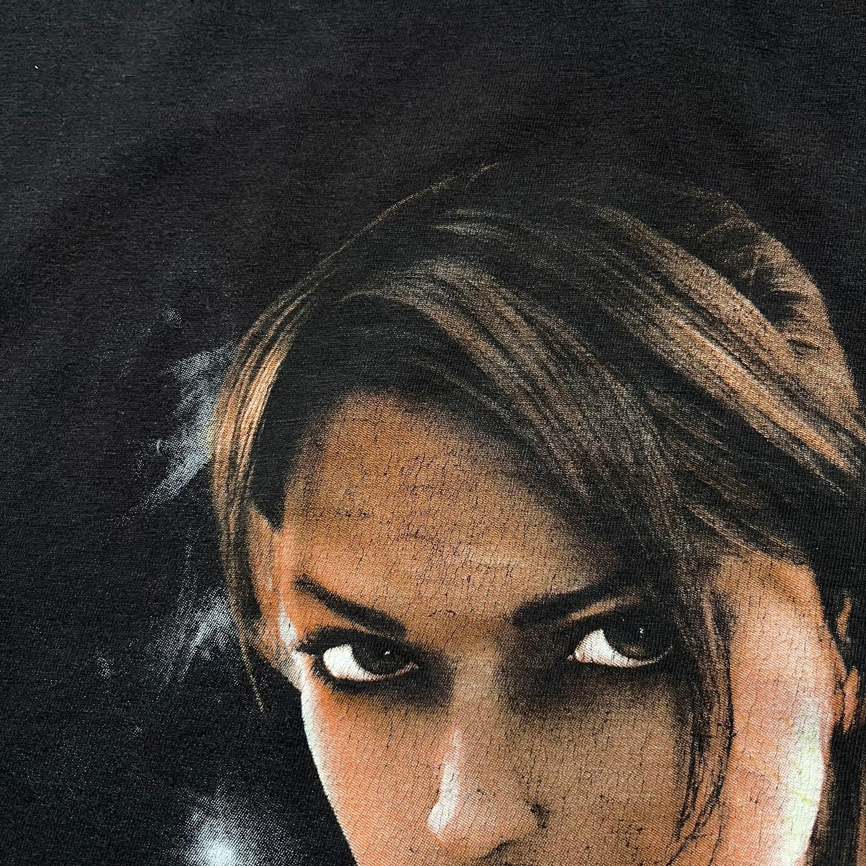 Tomb Raider Lara Croft 2006 Legend Tee is a black V-neck T-shirt made from 100% cotton on a Hanes blank. The front features the Lara Croft: Tomb Raider Legend cover graphic with Lara Croft’s face and the game title printed below. A white Eidos logo is printed on the sleeve, referencing the official game publisher.