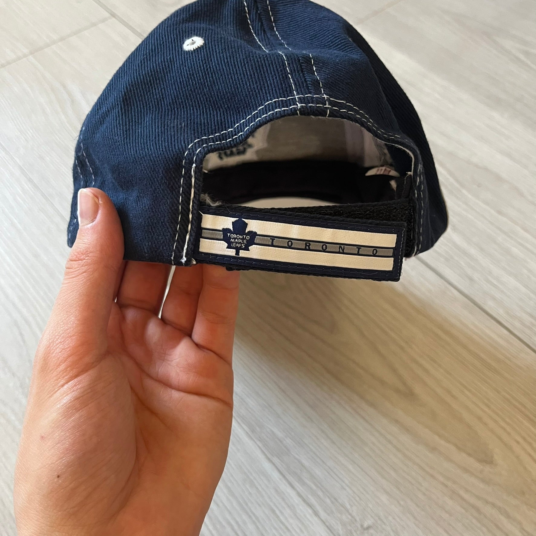 Hand holding a navy blue cap with a brand logo on a light wooden surface