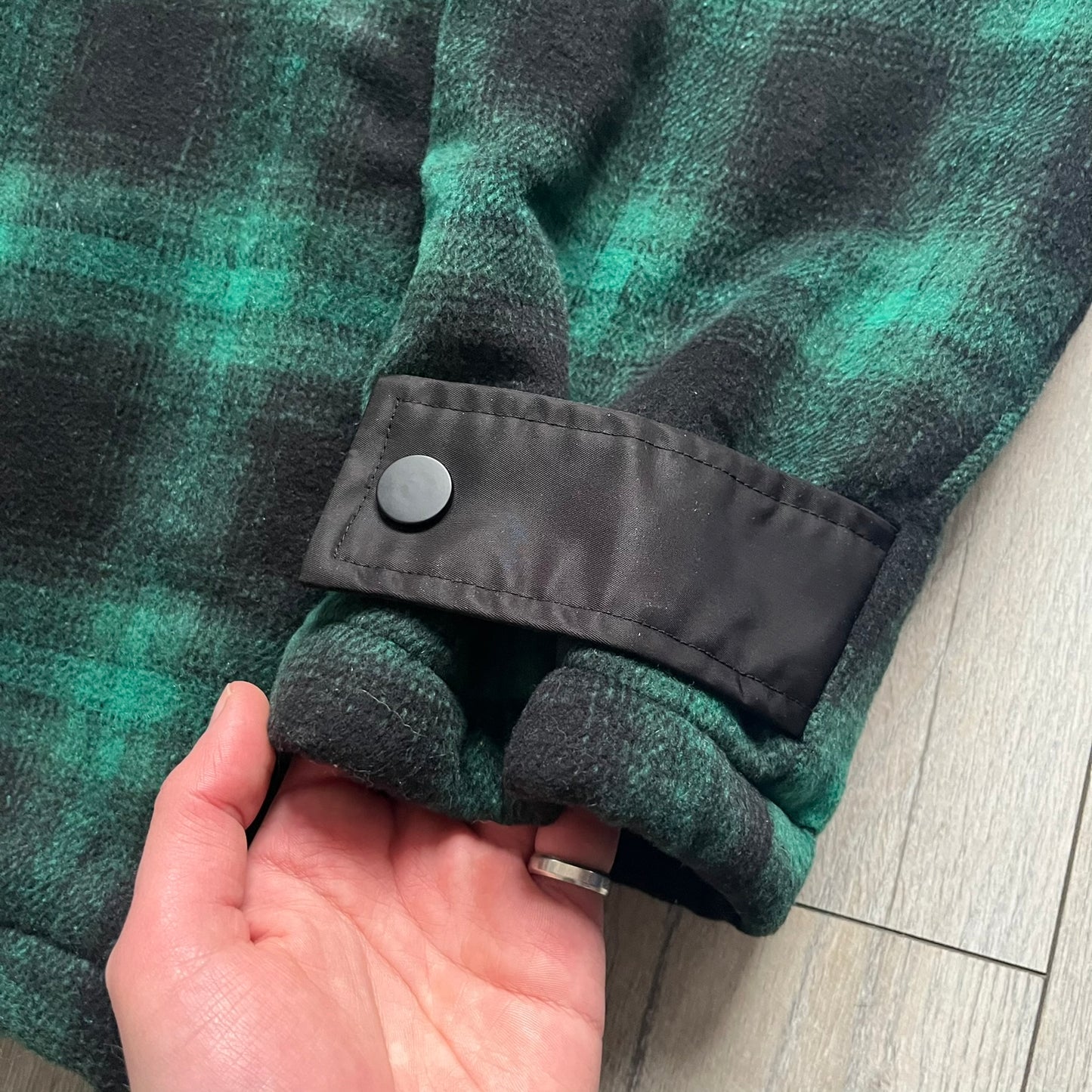 The Trapstar Irongate Green Plaid Lumberjack Jacket is a woven jacket in a green and black checked pattern, made from a 95% polyester and 5% wool outer with a full polyester lining. It features contrast shell panels at the shoulders, exposed popper fastenings at the front, a classic collar, and adjustable popper tabs at the cuffs. Details include side slip pockets, a Trapstar brand patch at the front hem, and a large Trapstar logo embroidered across the upper back yoke.
