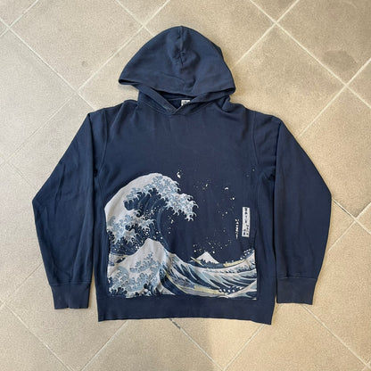 Uniqlo UT 2018 Hokusai The Great Wave Hoodie is a thick, dark navy hoodie featuring a large print of "The Great Wave off Kanagawa" by Hokusai across the lower front, created in collaboration with the Museum of Fine Arts Boston. It includes side pockets.