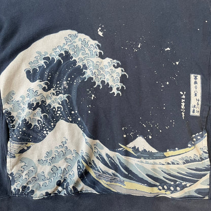Uniqlo UT 2018 Hokusai The Great Wave Hoodie is a thick, dark navy hoodie featuring a large print of "The Great Wave off Kanagawa" by Hokusai across the lower front, created in collaboration with the Museum of Fine Arts Boston. It includes side pockets.