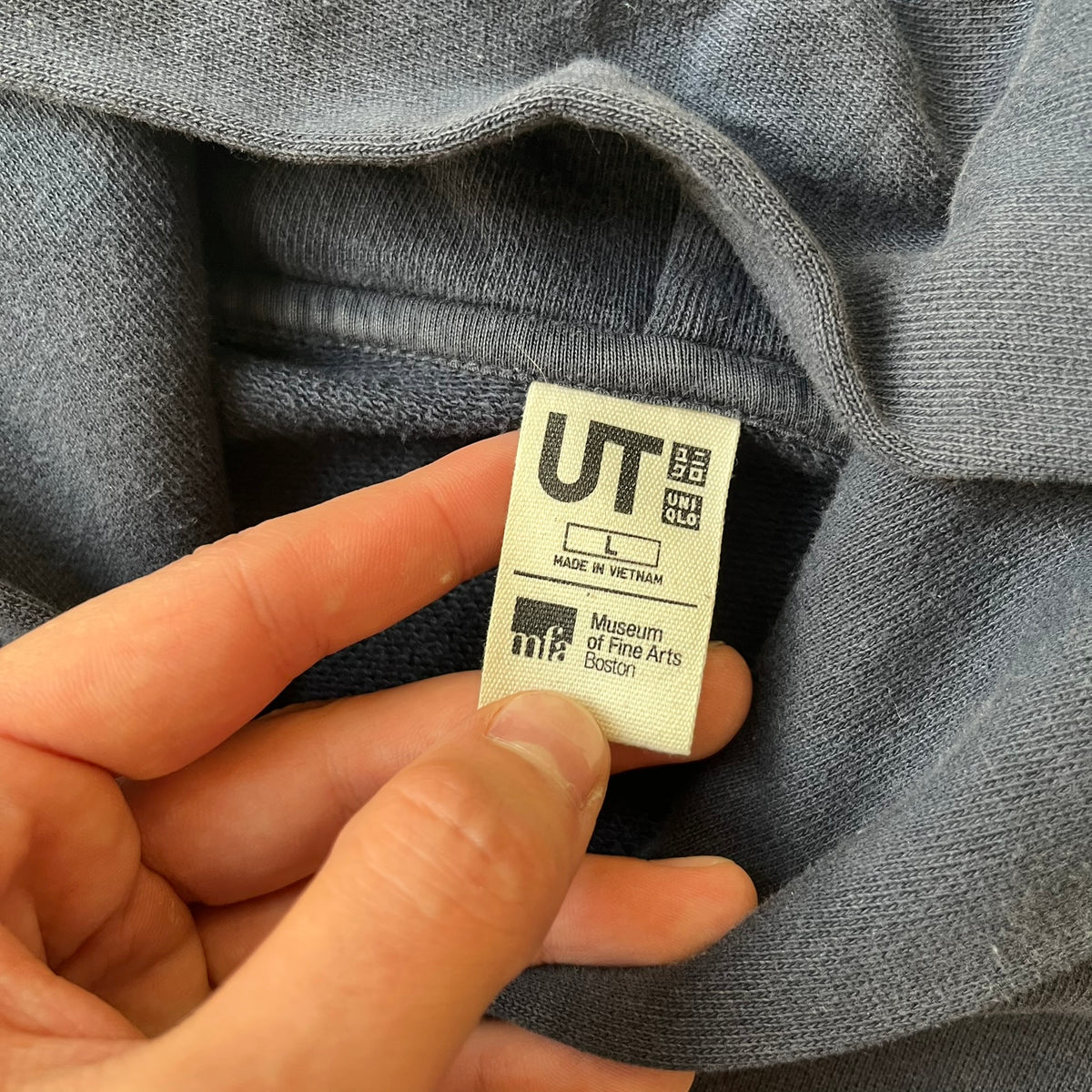 Uniqlo UT 2018 Hokusai The Great Wave Hoodie is a thick, dark navy hoodie featuring a large print of "The Great Wave off Kanagawa" by Hokusai across the lower front, created in collaboration with the Museum of Fine Arts Boston. It includes side pockets.