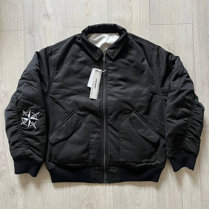 Unknown London Reversible Bomber Jacket crafted from padded polyester with a relaxed fit. One side features black matte fabric with embroidered logo, snakes, and multicolor detailing, plus arm patch and chest logo. The reverse side is beige with subtle chest embroidery in a softer cotton-like texture, offering two distinct styling options.