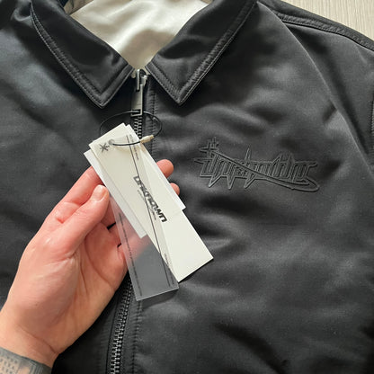 Unknown London Reversible Bomber Jacket crafted from padded polyester with a relaxed fit. One side features black matte fabric with embroidered logo, snakes, and multicolor detailing, plus arm patch and chest logo. The reverse side is beige with subtle chest embroidery in a softer cotton-like texture, offering two distinct styling options.