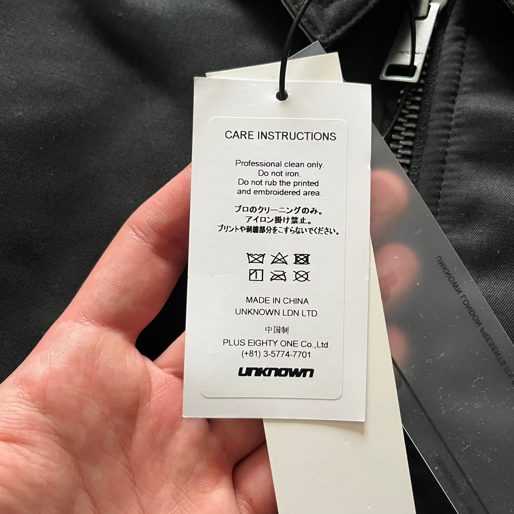 Unknown London Reversible Bomber Jacket crafted from padded polyester with a relaxed fit. One side features black matte fabric with embroidered logo, snakes, and multicolor detailing, plus arm patch and chest logo. The reverse side is beige with subtle chest embroidery in a softer cotton-like texture, offering two distinct styling options.