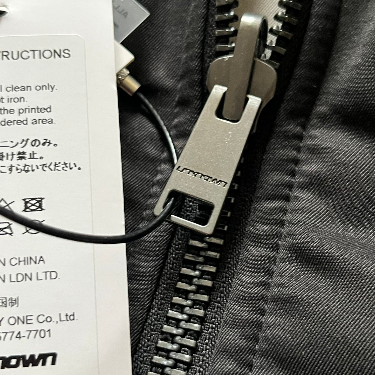 Unknown London Reversible Bomber Jacket crafted from padded polyester with a relaxed fit. One side features black matte fabric with embroidered logo, snakes, and multicolor detailing, plus arm patch and chest logo. The reverse side is beige with subtle chest embroidery in a softer cotton-like texture, offering two distinct styling options.