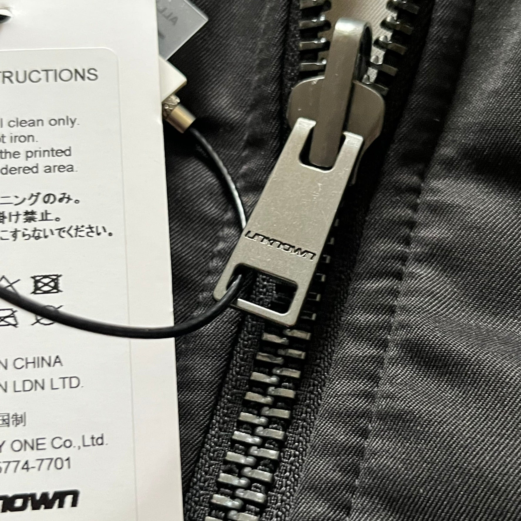 Unknown London Reversible Bomber Jacket crafted from padded polyester with a relaxed fit. One side features black matte fabric with embroidered logo, snakes, and multicolor detailing, plus arm patch and chest logo. The reverse side is beige with subtle chest embroidery in a softer cotton-like texture, offering two distinct styling options.