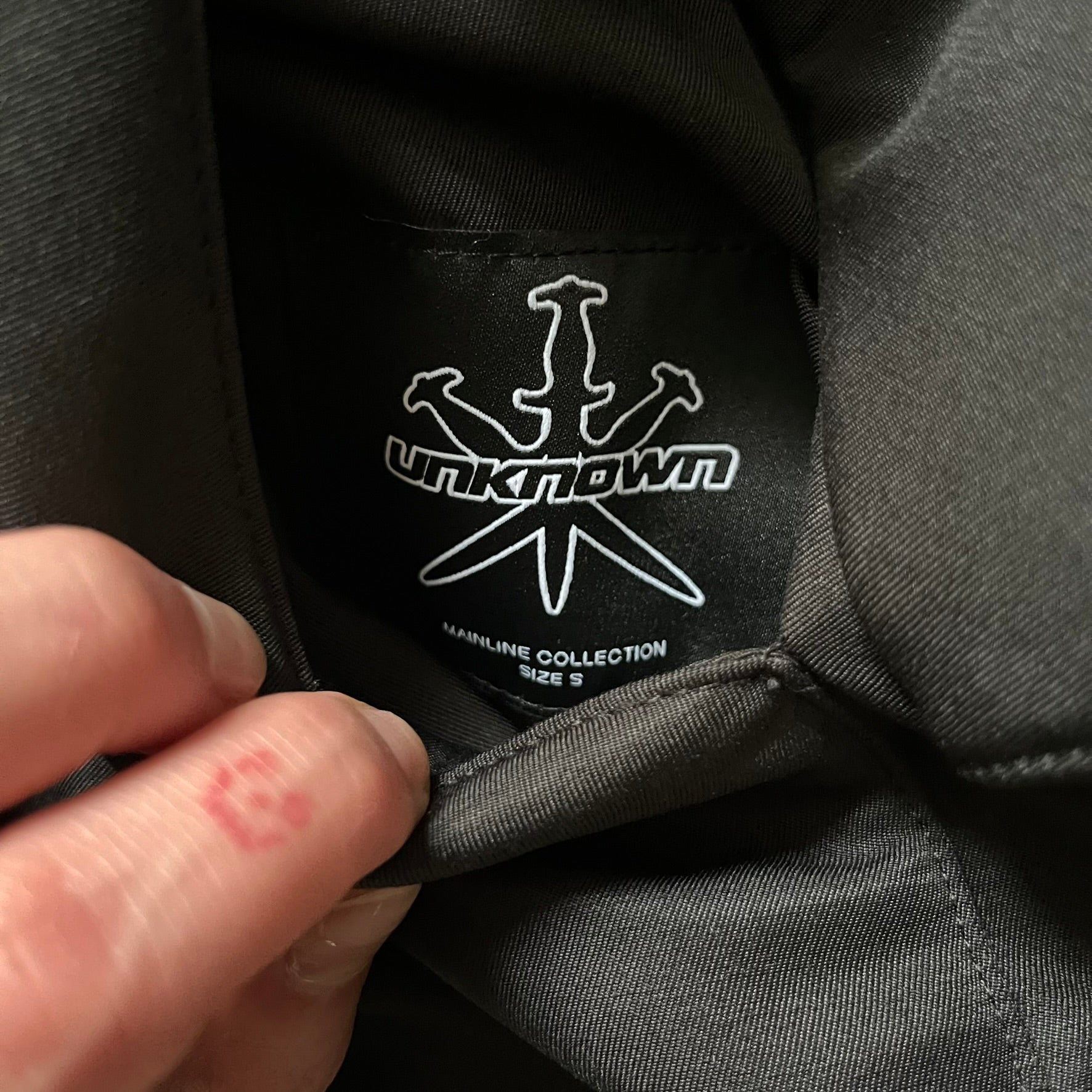 Unknown London Reversible Bomber Jacket crafted from padded polyester with a relaxed fit. One side features black matte fabric with embroidered logo, snakes, and multicolor detailing, plus arm patch and chest logo. The reverse side is beige with subtle chest embroidery in a softer cotton-like texture, offering two distinct styling options.