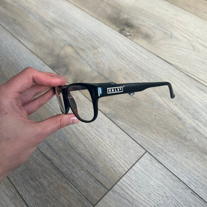 Valve Black Promo Eyeglasses are non-prescription promotional glasses featuring simple black plastic frames with clear zero-strength lenses. Small white Valve logos are placed on both sides of the frame arms. The design is minimal and intended as branded promotional eyewear.