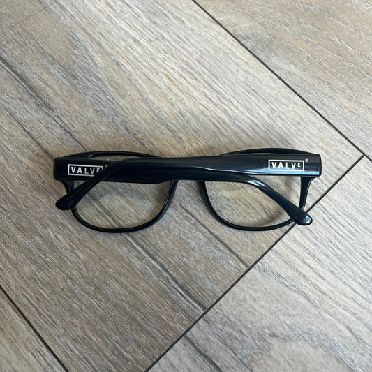 Valve Black Promo Eyeglasses are non-prescription promotional glasses featuring simple black plastic frames with clear zero-strength lenses. Small white Valve logos are placed on both sides of the frame arms. The design is minimal and intended as branded promotional eyewear.