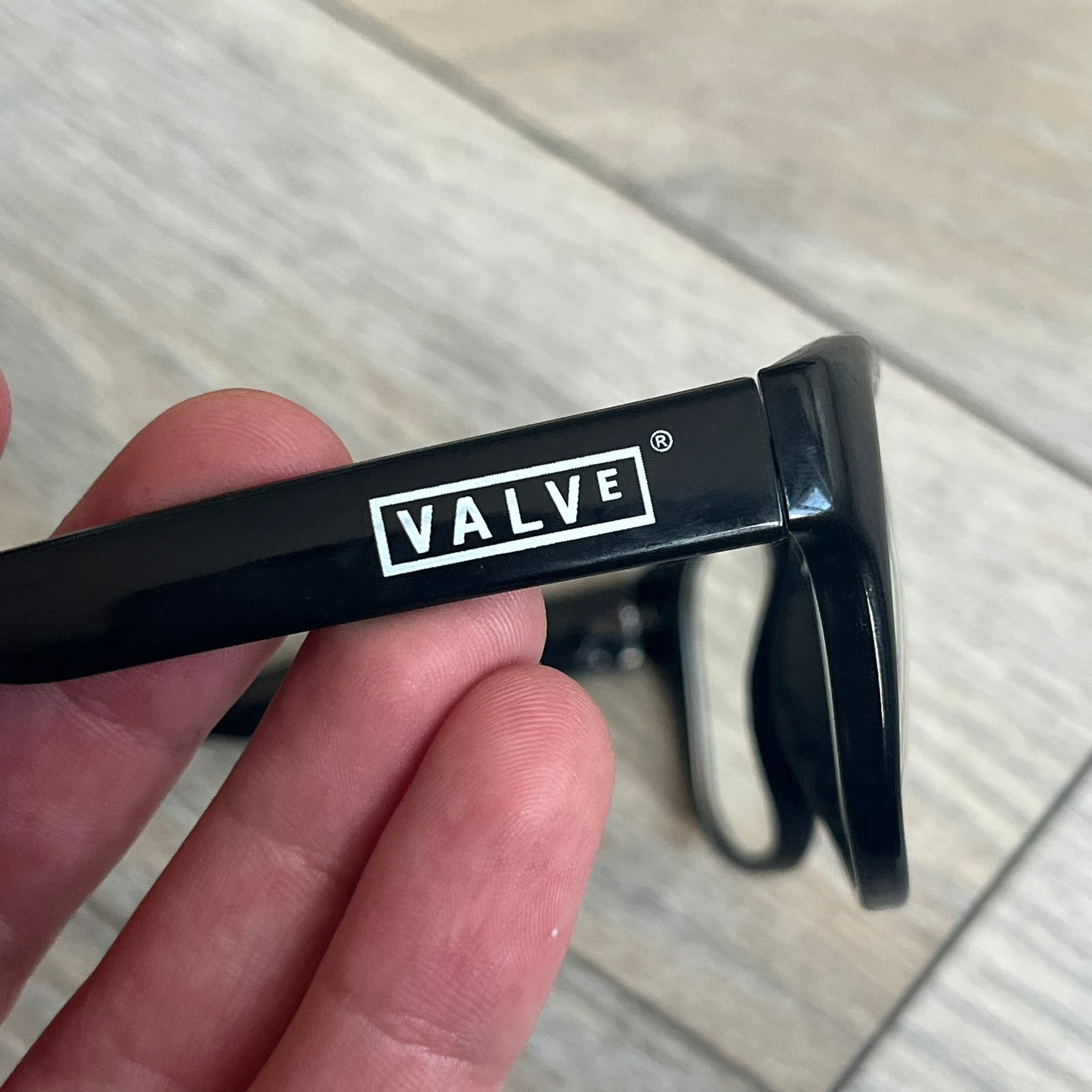 Valve Black Promo Eyeglasses are non-prescription promotional glasses featuring simple black plastic frames with clear zero-strength lenses. Small white Valve logos are placed on both sides of the frame arms. The design is minimal and intended as branded promotional eyewear.