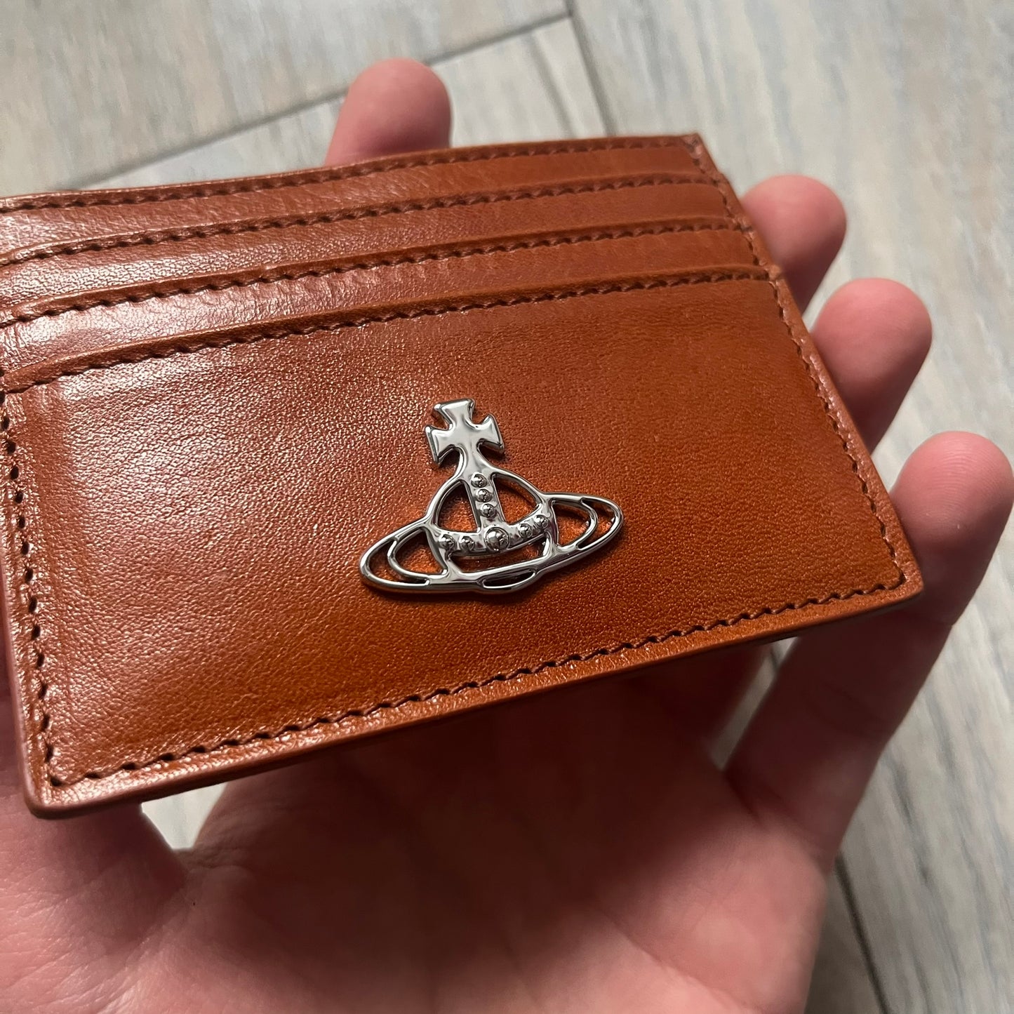 Vivienne Westwood Brown Flat Card Holder is crafted from buffed leather in a camel brown tone with logo hardware at the front. It features four card slots, a central note compartment, black twill lining, and an interior leather Vivienne Westwood tab with a material tag. Made in Italy, the card holder comes with the original box and tags. 252314M163098