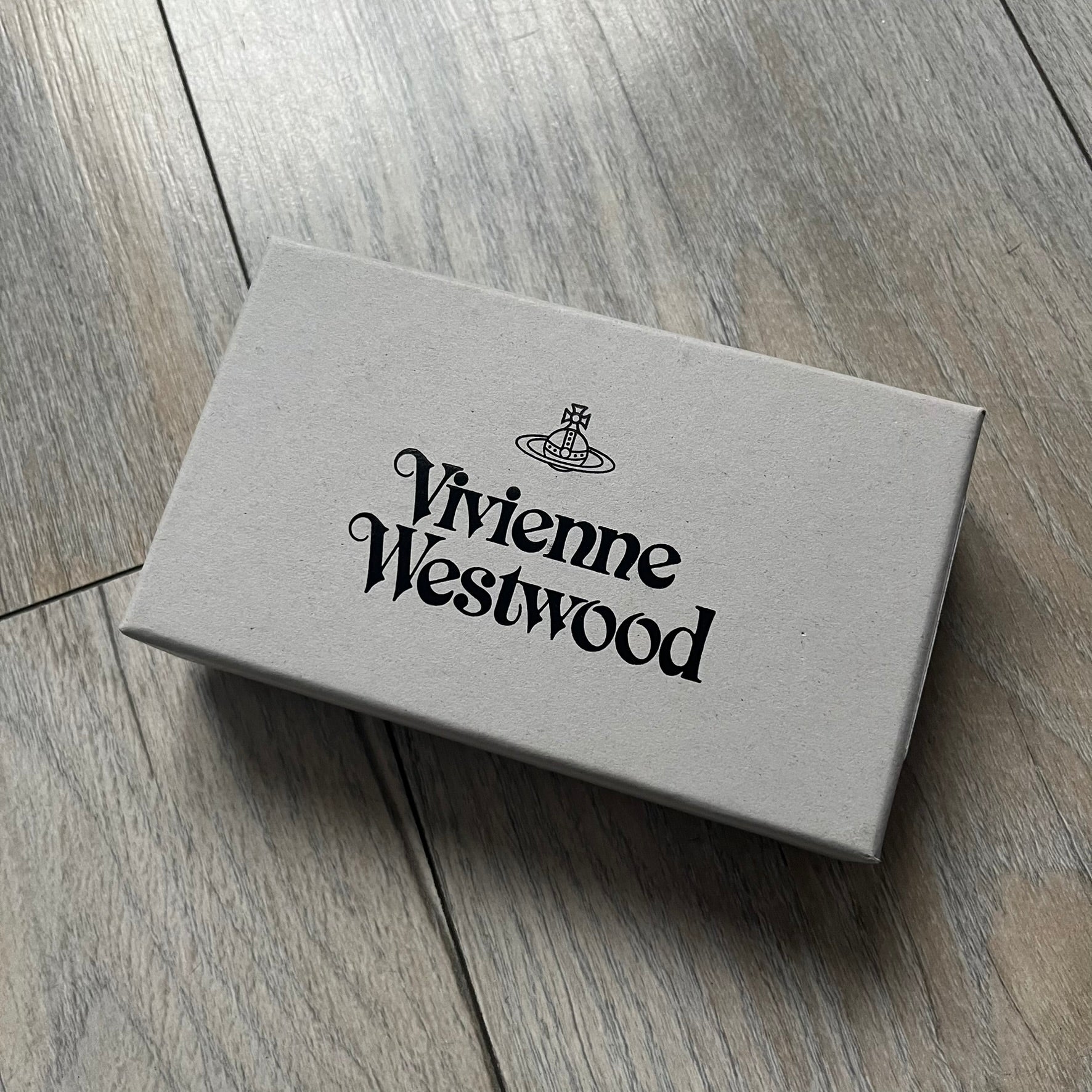 Vivienne Westwood Brown Flat Card Holder is crafted from buffed leather in a camel brown tone with logo hardware at the front. It features four card slots, a central note compartment, black twill lining, and an interior leather Vivienne Westwood tab with a material tag. Made in Italy, the card holder comes with the original box and tags. 252314M163098