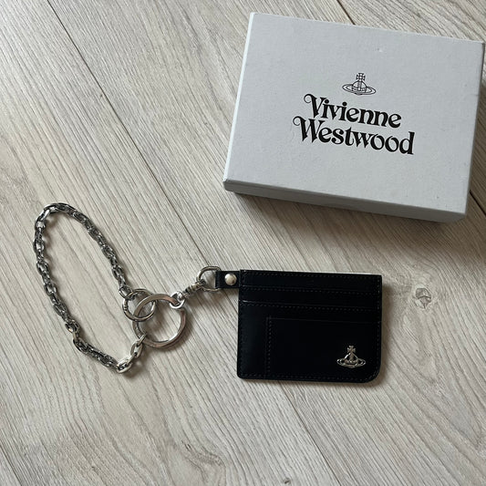 Vivienne Westwood Flat Chain Card Holder in black leather, featuring the signature silver Orb emblem on the corner. Designed with four compartments - three main slots and one smaller front pocket. Completed with a flat chain and an engraved Vivienne Westwood loop for a refined finish.