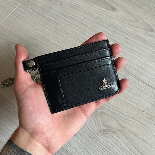 Vivienne Westwood Flat Chain Card Holder in black leather, featuring the signature silver Orb emblem on the corner. Designed with four compartments - three main slots and one smaller front pocket. Completed with a flat chain and an engraved Vivienne Westwood loop for a refined finish.
