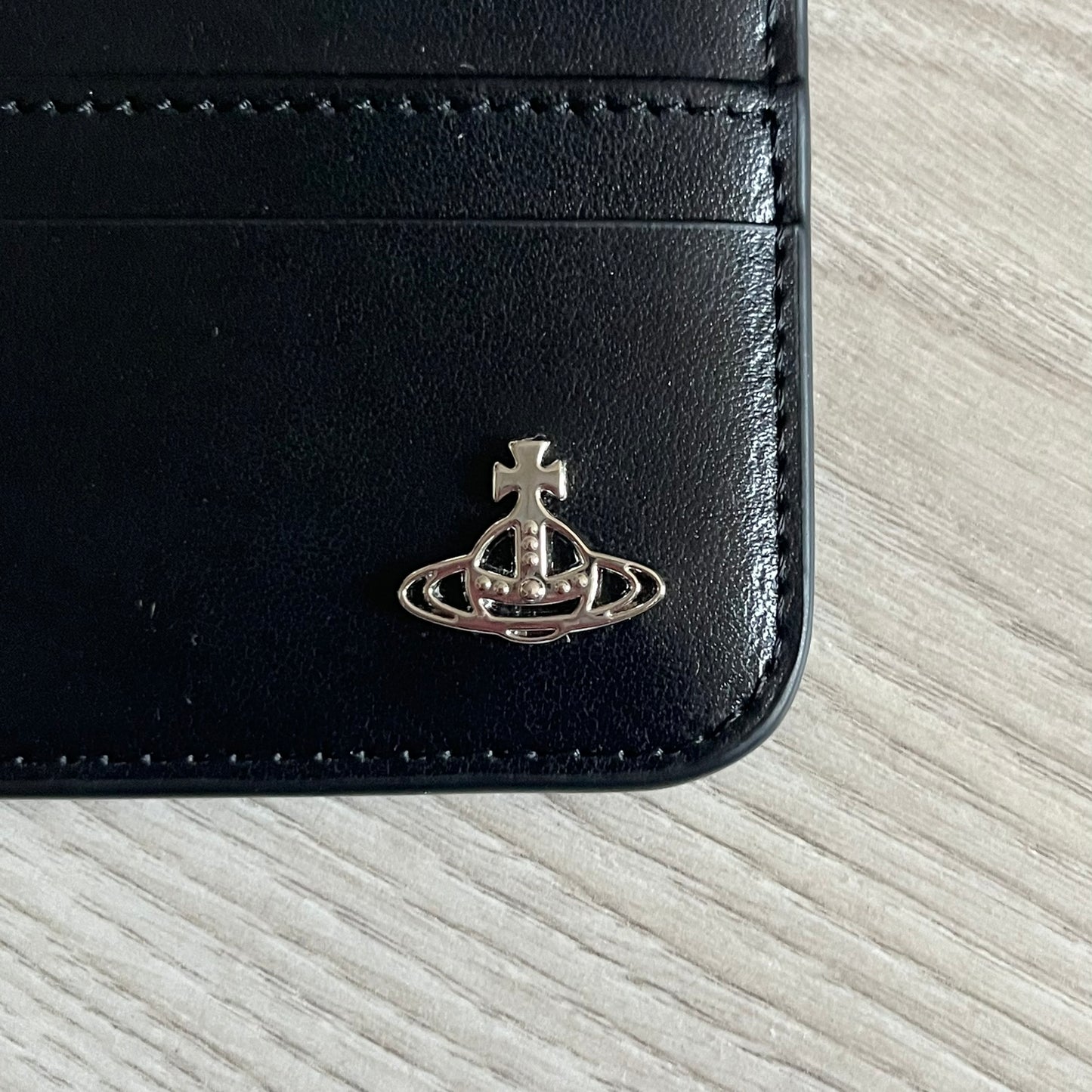 Vivienne Westwood Flat Chain Card Holder in black leather, featuring the signature silver Orb emblem on the corner. Designed with four compartments - three main slots and one smaller front pocket. Completed with a flat chain and an engraved Vivienne Westwood loop for a refined finish.
