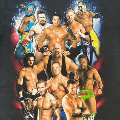 WWE 2011 All Over Print Promo Tee is a black short-sleeve T-shirt featuring a large front graphic of multiple WWE wrestlers, including Rey Mysterio, John Cena, and Randy Orton. A small WWE logo is printed beneath the main graphic. The shirt has no neck tag and was released as official promotional merchandise in 2011.