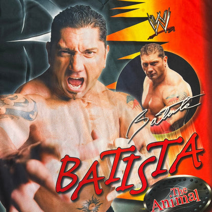 WWE Batista 2007 Kalciomania AOP Tee features an all-over print design with red, black, and white graphics throughout. The front includes Two Batista graphics with red&nbsp; “Batista” text, WWE logos, and additional printed details. The back features Batista with Unleashed Batista text graphic. The sleeves include a WWE logo and branding. Finished with a Kalciomania licensed tag.