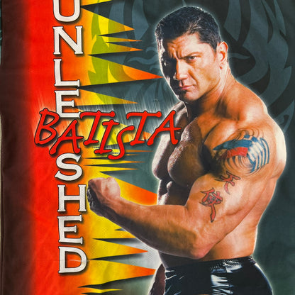 WWE Batista 2007 Kalciomania AOP Tee features an all-over print design with red, black, and white graphics throughout. The front includes Two Batista graphics with red&nbsp; “Batista” text, WWE logos, and additional printed details. The back features Batista with Unleashed Batista text graphic. The sleeves include a WWE logo and branding. Finished with a Kalciomania licensed tag.