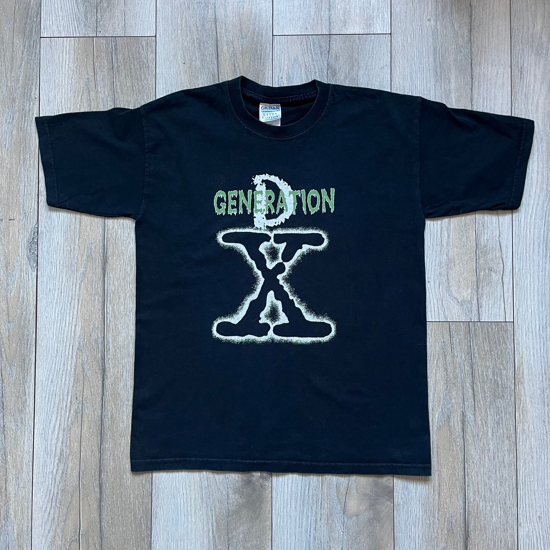 WWE D-Generation X 2000s Black Tee is a black short-sleeve T-shirt made on a Gildan blank in the early 2000s. The front features a D-Generation X logo with a large black “X” outlined in white glow and subtle green, topped with white “D” and green “Generation” text. This shirt was released as official WWE merchandise during the 2000s.