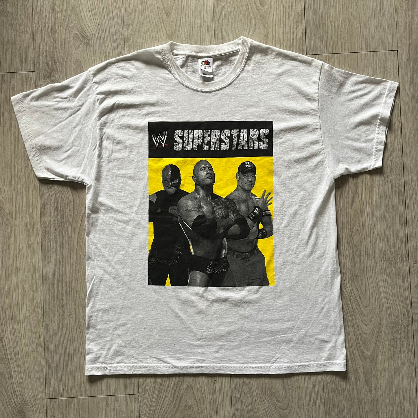 Vintage WWE Superstars Tee in white, highlighted by a large front print of wrestling icons The Rock, Rey Mysterio, and John Cena over a yellow base. Features the WWE logo and “Superstars” branding, printed on a Fruit of the Loom blank.