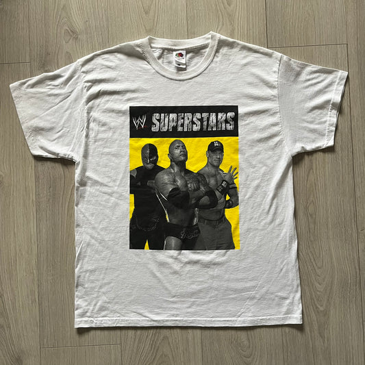 Vintage WWE Superstars Tee in white, highlighted by a large front print of wrestling icons The Rock, Rey Mysterio, and John Cena over a yellow base. Features the WWE logo and “Superstars” branding, printed on a Fruit of the Loom blank.