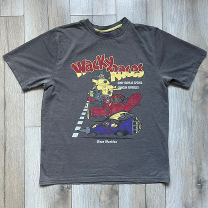 Wacky Races Gray 2010 Tee is a short-sleeve t-shirt featuring a front graphic with red and yellow “Wacky Races” text at the top. The design shows three cars at the starting line: the Army Surplus Special, the Crimson Haybaler, and the Mean Machine, each labeled with small white text next to the vehicles. The tee includes a purple Wacky Races neck tag with Cartoon Network 2010 licensing.
