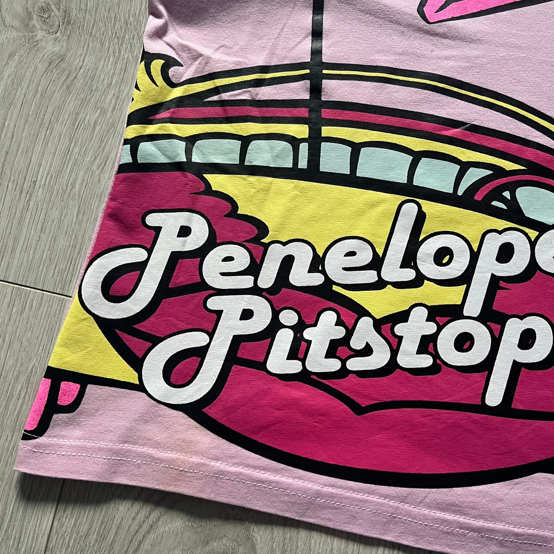 Baby pink 2013 Wacky Races women’s tee with Penelope Pitstop and her iconic "The Compact Pussycat" car. Glittery pink accents on her helmet, skirt, umbrella with white “Penelope Pitstop!” text. Officially Hanna-Barbera licensed.