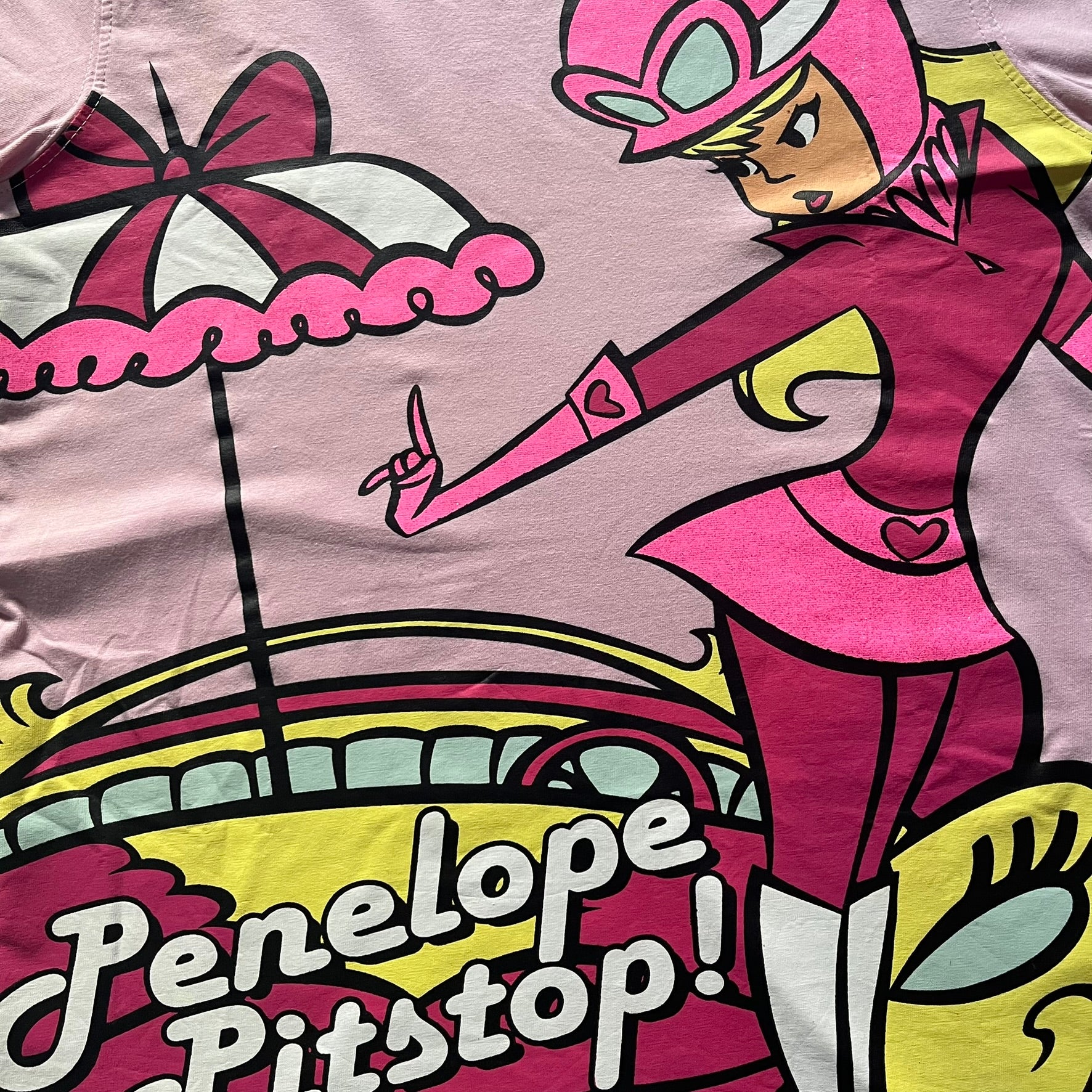Baby pink 2013 Wacky Races women’s tee with Penelope Pitstop and her iconic "The Compact Pussycat" car. Glittery pink accents on her helmet, skirt, umbrella with white “Penelope Pitstop!” text. Officially Hanna-Barbera licensed.