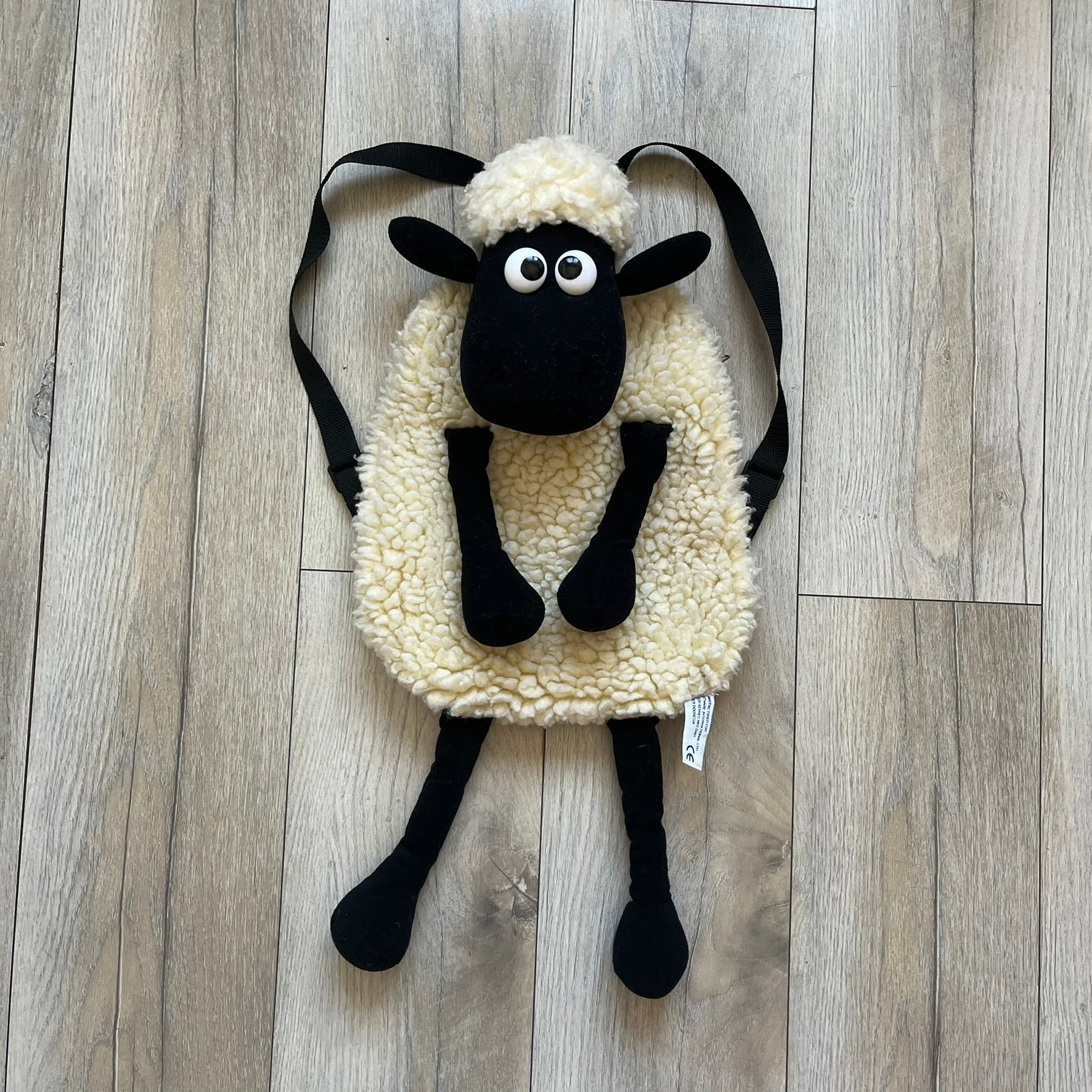 Wallace &amp; Gromit “Shaun The Sheep” 1990’s Backpack is a character-shaped backpack designed as Shaun the Sheep with black shoulder straps running from the bottom to the top of the body. The arms, legs, and ears are movable, and the face features plastic eyes. It includes one large main storage compartment, and a tag dating to the late 1980s-1990s production period.