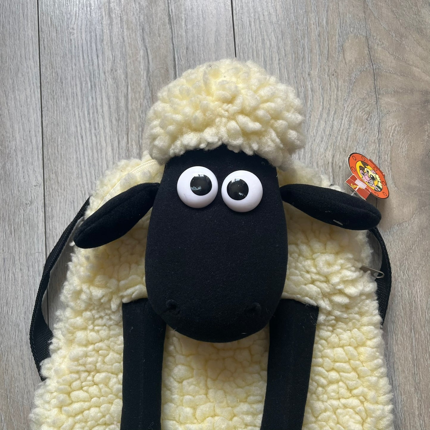 Wallace &amp; Gromit “Shaun The Sheep” 1990’s Backpack is a character-shaped backpack designed as Shaun the Sheep with black shoulder straps running from the bottom to the top of the body. The arms, legs, and ears are movable, and the face features plastic eyes. It includes a Wallace &amp; Gromit paper tag, a material tag, and one large main storage compartment, dating to the late 1980s-1990s production period.