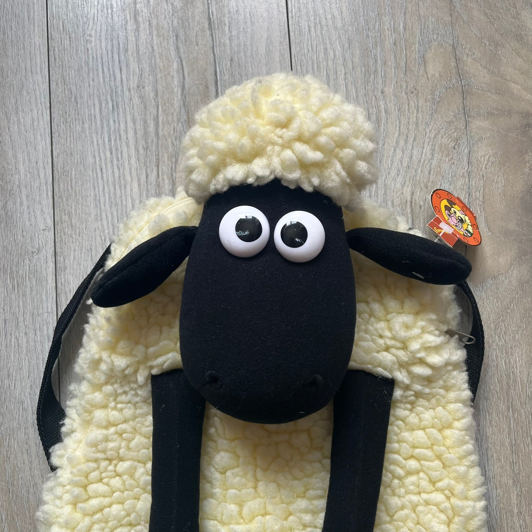 Wallace &amp; Gromit “Shaun The Sheep” 1990’s Backpack is a character-shaped backpack designed as Shaun the Sheep with black shoulder straps running from the bottom to the top of the body. The arms, legs, and ears are movable, and the face features plastic eyes. It includes a Wallace &amp; Gromit paper tag, a material tag, and one large main storage compartment, dating to the late 1980s-1990s production period.