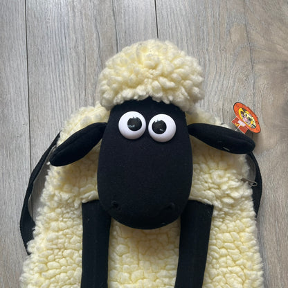 Wallace &amp; Gromit “Shaun The Sheep” 1990’s Backpack is a character-shaped backpack designed as Shaun the Sheep with black shoulder straps running from the bottom to the top of the body. The arms, legs, and ears are movable, and the face features plastic eyes. It includes a Wallace &amp; Gromit paper tag, a material tag, and one large main storage compartment, dating to the late 1980s-1990s production period.