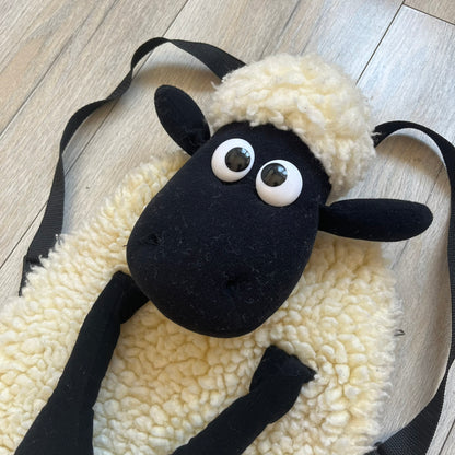Wallace &amp; Gromit “Shaun The Sheep” 1990’s Backpack is a character-shaped backpack designed as Shaun the Sheep with black shoulder straps running from the bottom to the top of the body. The arms, legs, and ears are movable, and the face features plastic eyes. It includes one large main storage compartment, and a tag dating to the late 1980s-1990s production period.