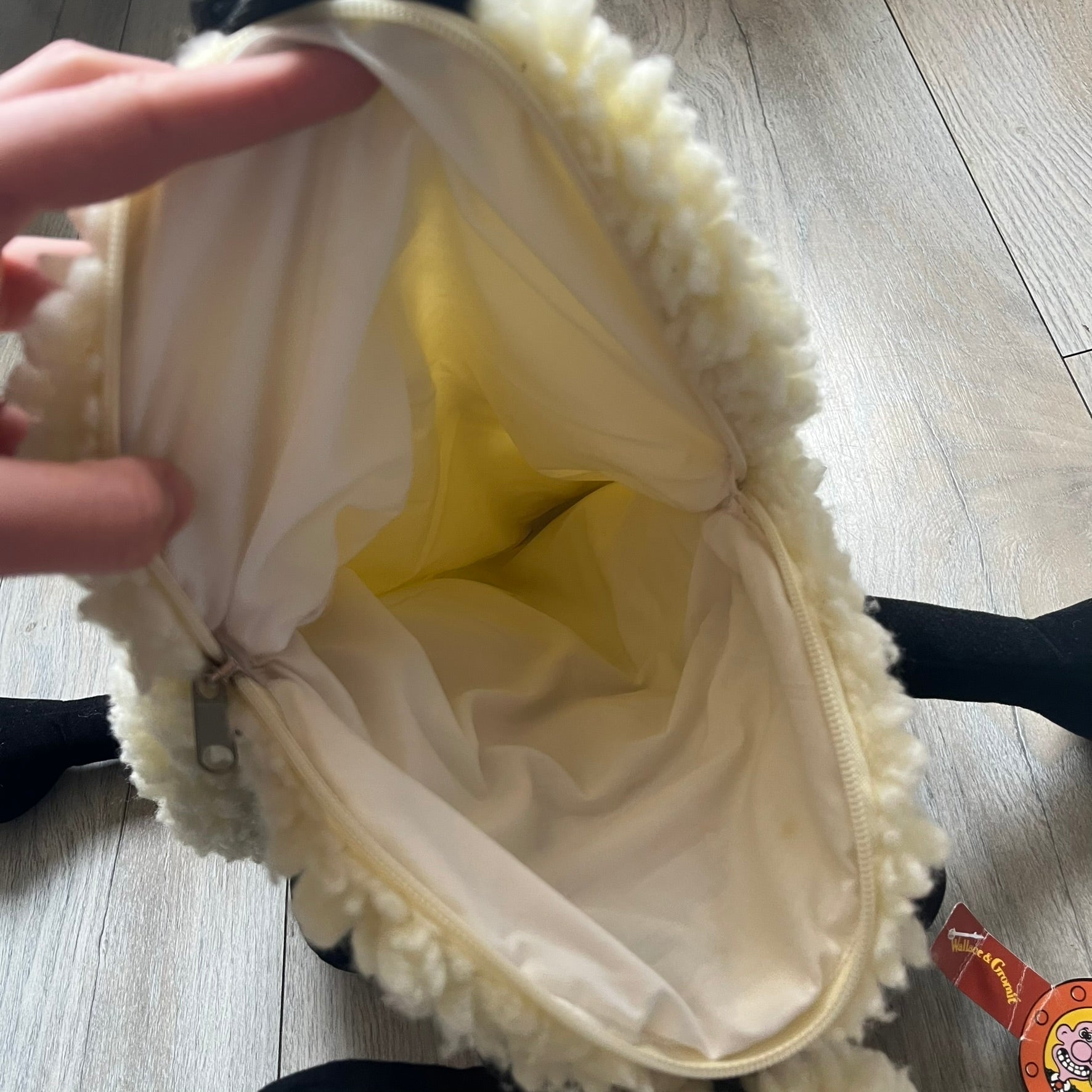 Wallace &amp; Gromit “Shaun The Sheep” 1990’s Backpack is a character-shaped backpack designed as Shaun the Sheep with black shoulder straps running from the bottom to the top of the body. The arms, legs, and ears are movable, and the face features plastic eyes. It includes a Wallace &amp; Gromit paper tag, a material tag, and one large main storage compartment, dating to the late 1980s-1990s production period.