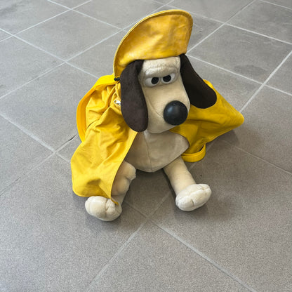 The Wallace and Gromit Gromit Plush Backpack is a 1990s licensed item produced by Aardman Animations. It features Gromit dressed in his bright yellow PVC raincoat and matching hat, as seen in The Wrong Trousers. The backpack is made from soft plush fabric with plastic eyes, a hard black nose, and a genuine stamp confirming official production. The bag opens from the side and includes adjustable shoulder straps for wearability.