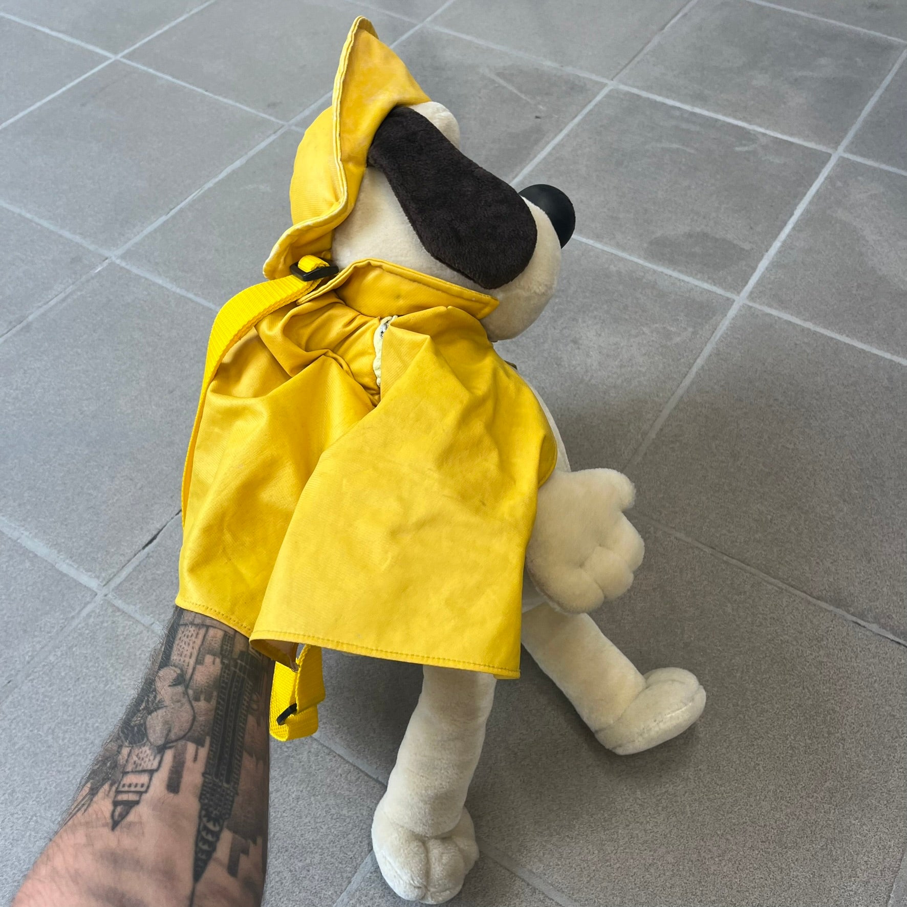 The Wallace and Gromit Gromit Plush Backpack is a 1990s licensed item produced by Aardman Animations. It features Gromit dressed in his bright yellow PVC raincoat and matching hat, as seen in The Wrong Trousers. The backpack is made from soft plush fabric with plastic eyes, a hard black nose, and a genuine stamp confirming official production. The bag opens from the side and includes adjustable shoulder straps for wearability.