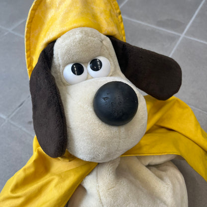 The Wallace and Gromit Gromit Plush Backpack is a 1990s licensed item produced by Aardman Animations. It features Gromit dressed in his bright yellow PVC raincoat and matching hat, as seen in The Wrong Trousers. The backpack is made from soft plush fabric with plastic eyes, a hard black nose, and a genuine stamp confirming official production. The bag opens from the side and includes adjustable shoulder straps for wearability.