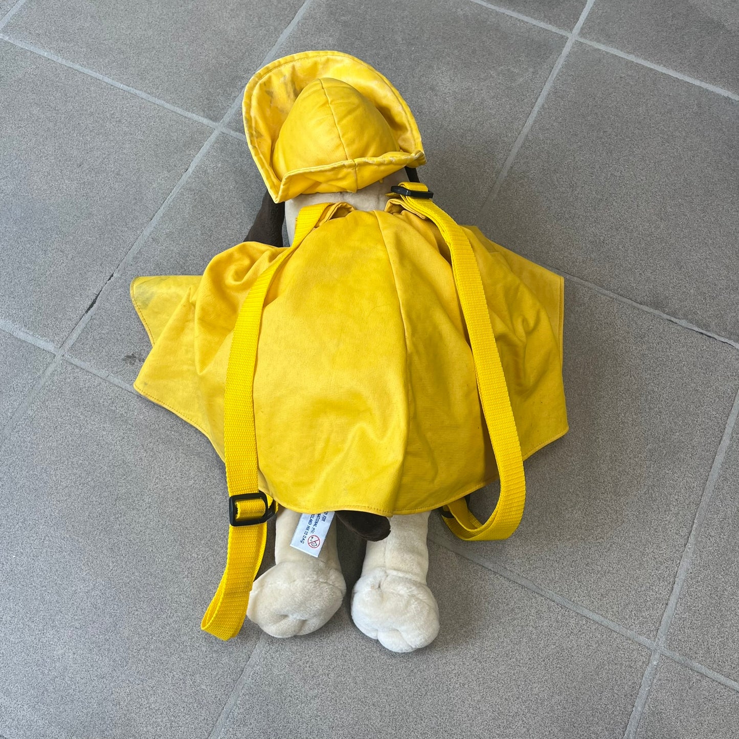 The Wallace and Gromit Gromit Plush Backpack is a 1990s licensed item produced by Aardman Animations. It features Gromit dressed in his bright yellow PVC raincoat and matching hat, as seen in The Wrong Trousers. The backpack is made from soft plush fabric with plastic eyes, a hard black nose, and a genuine stamp confirming official production. The bag opens from the side and includes adjustable shoulder straps for wearability.