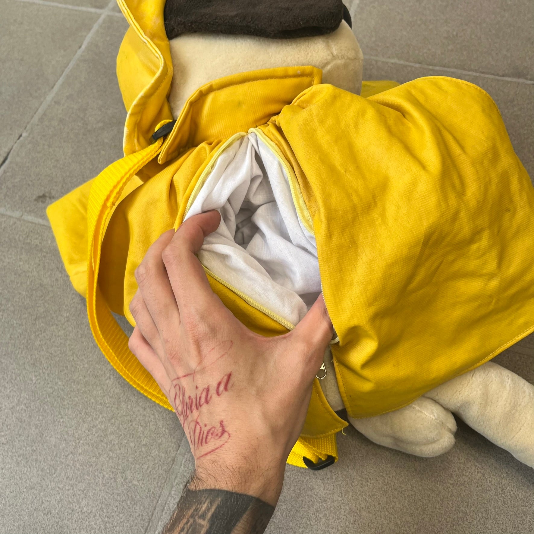 The Wallace and Gromit Gromit Plush Backpack is a 1990s licensed item produced by Aardman Animations. It features Gromit dressed in his bright yellow PVC raincoat and matching hat, as seen in The Wrong Trousers. The backpack is made from soft plush fabric with plastic eyes, a hard black nose, and a genuine stamp confirming official production. The bag opens from the side and includes adjustable shoulder straps for wearability.
