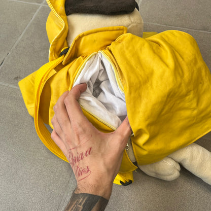 The Wallace and Gromit Gromit Plush Backpack is a 1990s licensed item produced by Aardman Animations. It features Gromit dressed in his bright yellow PVC raincoat and matching hat, as seen in The Wrong Trousers. The backpack is made from soft plush fabric with plastic eyes, a hard black nose, and a genuine stamp confirming official production. The bag opens from the side and includes adjustable shoulder straps for wearability.