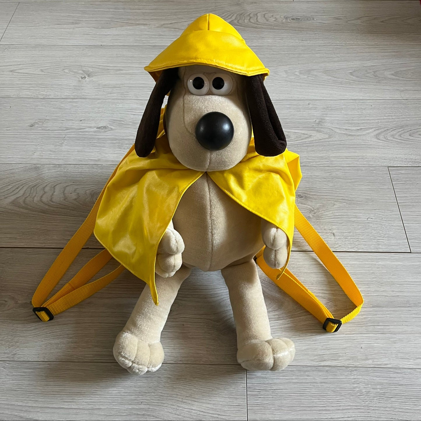 The Wallace and Gromit Gromit Plush Backpack is a 1990s licensed item produced by Aardman Animations. It features Gromit dressed in his bright yellow PVC raincoat and matching hat, as seen in The Wrong Trousers. The backpack is made from soft plush fabric with plastic eyes, a hard black nose, and a genuine stamp confirming official production. The bag opens from the side and includes adjustable shoulder straps for wearability