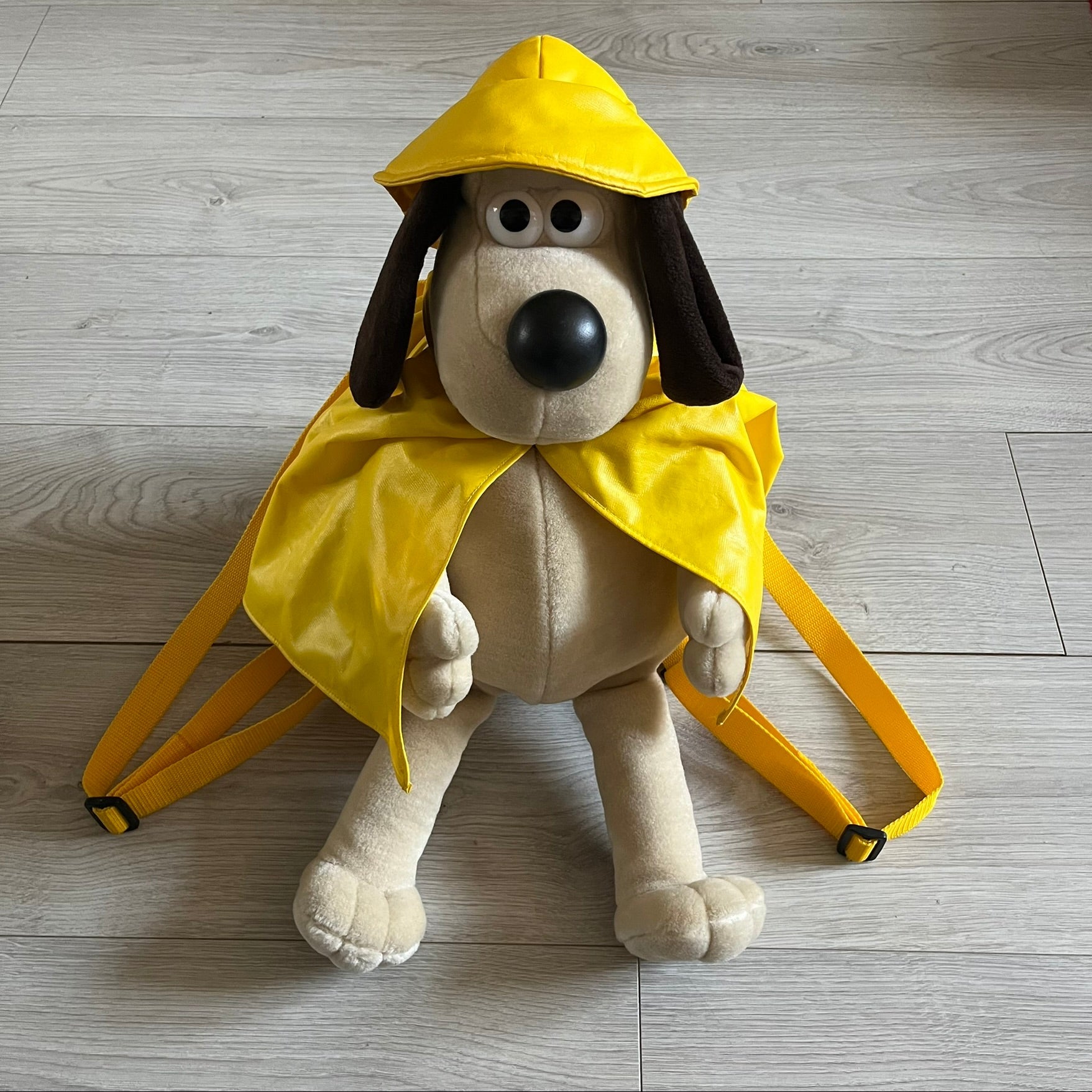 The Wallace and Gromit Gromit Plush Backpack is a 1990s licensed item produced by Aardman Animations. It features Gromit dressed in his bright yellow PVC raincoat and matching hat, as seen in The Wrong Trousers. The backpack is made from soft plush fabric with plastic eyes, a hard black nose, and a genuine stamp confirming official production. The bag opens from the side and includes adjustable shoulder straps for wearability
