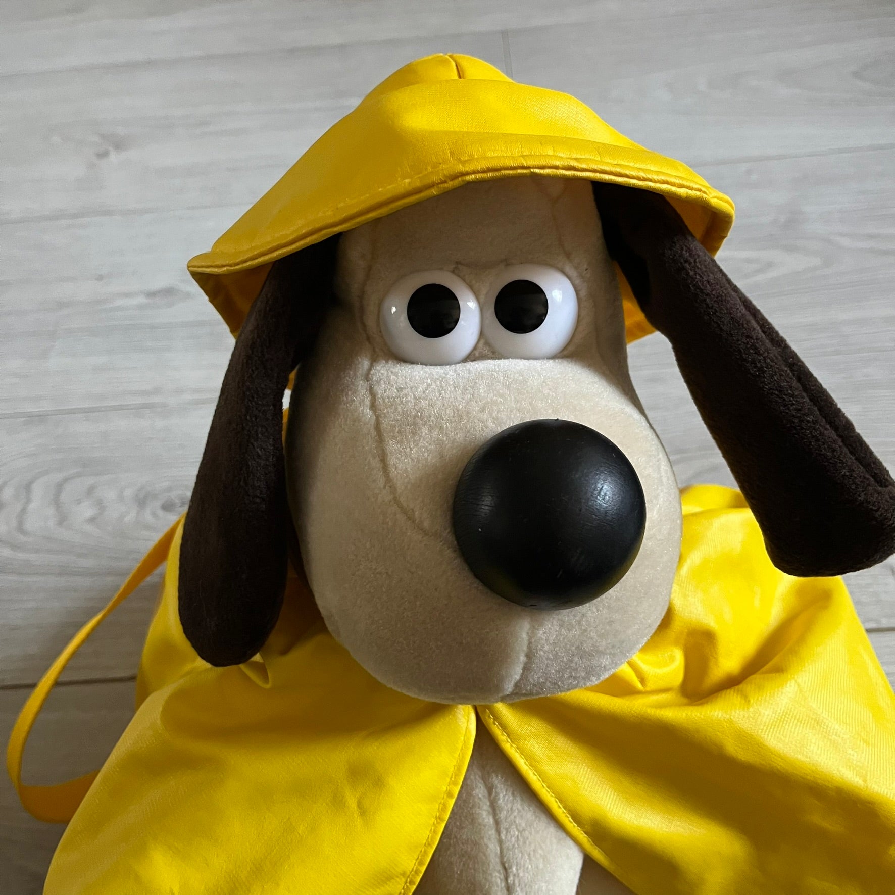 The Wallace and Gromit Gromit Plush Backpack is a 1990s licensed item produced by Aardman Animations. It features Gromit dressed in his bright yellow PVC raincoat and matching hat, as seen in The Wrong Trousers. The backpack is made from soft plush fabric with plastic eyes, a hard black nose, and a genuine stamp confirming official production. The bag opens from the side and includes adjustable shoulder straps for wearability