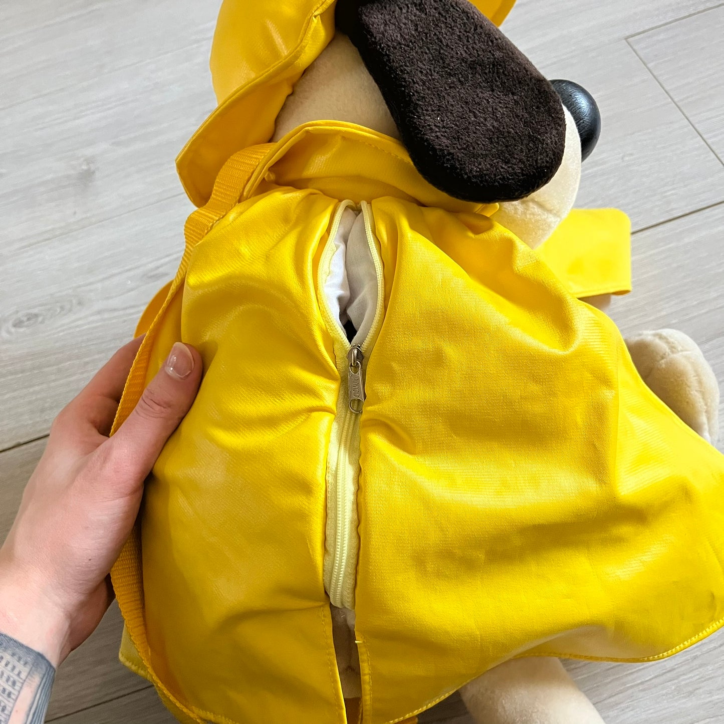 The Wallace and Gromit Gromit Plush Backpack is a 1990s licensed item produced by Aardman Animations. It features Gromit dressed in his bright yellow PVC raincoat and matching hat, as seen in The Wrong Trousers. The backpack is made from soft plush fabric with plastic eyes, a hard black nose, and a genuine stamp confirming official production. The bag opens from the side and includes adjustable shoulder straps for wearability