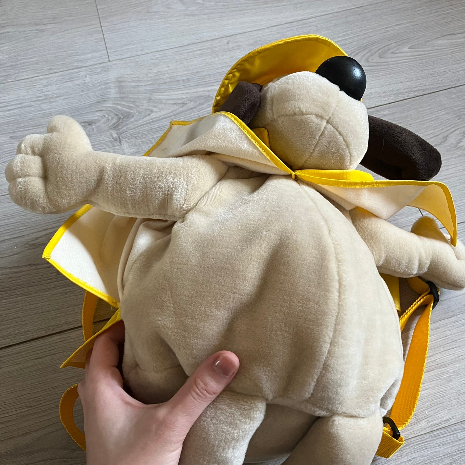 The Wallace and Gromit Gromit Plush Backpack is a 1990s licensed item produced by Aardman Animations. It features Gromit dressed in his bright yellow PVC raincoat and matching hat, as seen in The Wrong Trousers. The backpack is made from soft plush fabric with plastic eyes, a hard black nose, and a genuine stamp confirming official production. The bag opens from the side and includes adjustable shoulder straps for wearability